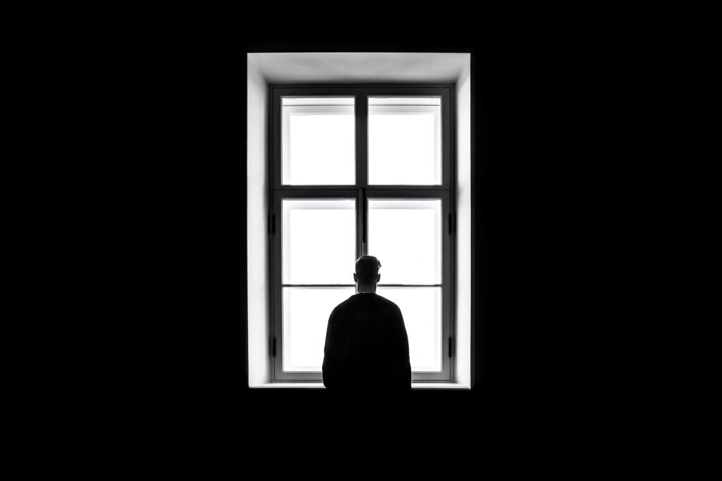 Man standing at window in dark, looking out